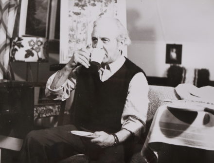 Der Künstler in seinem Atelier, mit einer Tasse Kaffee in der Hand schaut er auf die Staffelei.